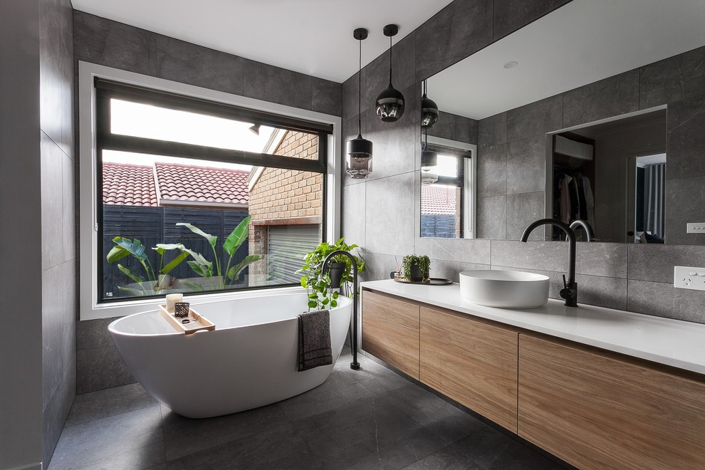 Inspiration for a mid-sized modern master bathroom in Melbourne with open cabinets, medium wood cabinets, a freestanding tub, a corner shower, a two-piece toilet, gray tile, grey walls, a drop-in sink, engineered quartz benchtops, grey floor, a hinged shower door and white benchtops.