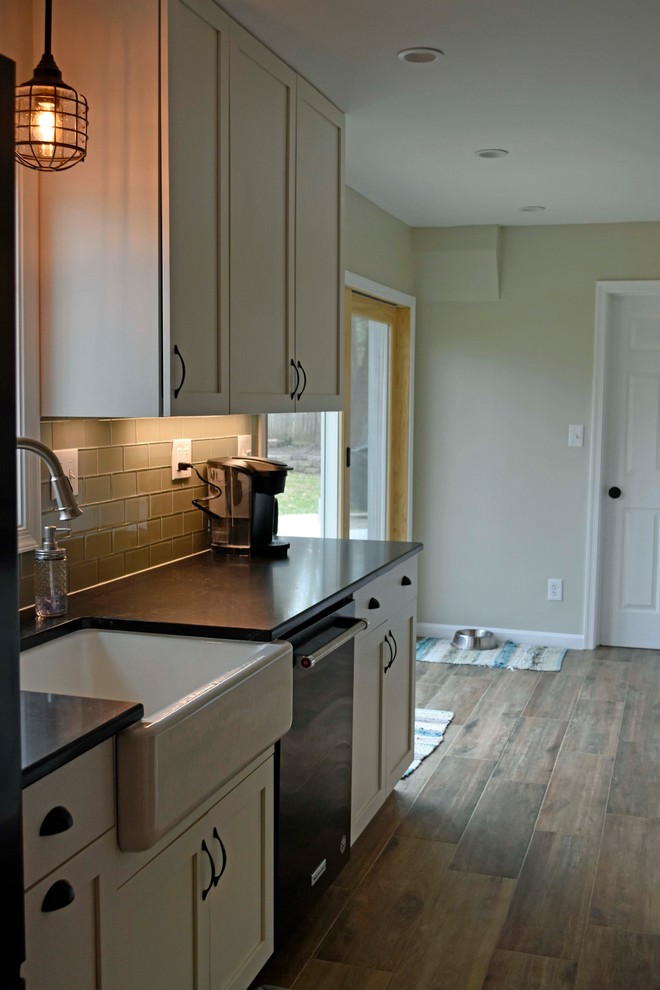 Example of a mid-sized transitional galley laminate floor and brown floor enclosed kitchen design in DC Metro with a farmhouse sink, shaker cabinets, white cabinets, granite countertops, gray backsplash, subway tile backsplash, stainless steel appliances, no island and black countertops