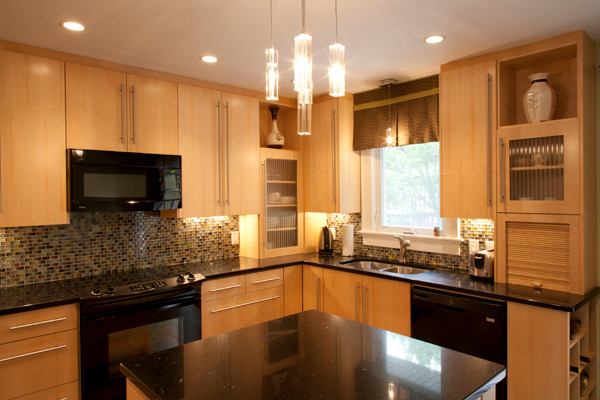 Example of a porcelain tile kitchen design with a double-bowl sink, raised-panel cabinets, light wood cabinets, multicolored backsplash, ceramic backsplash, black appliances and an island