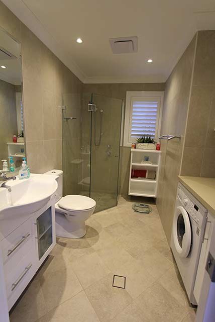 Photo of a modern bathroom in Sydney with flat-panel cabinets, white cabinets, a corner shower, a two-piece toilet, beige tile, an integrated sink, a hinged shower door and a laundry.