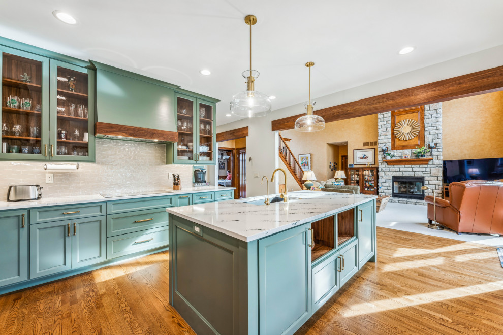 Photo of a large traditional l-shaped open plan kitchen in Columbus with an undermount sink, recessed-panel cabinets, green cabinets, quartz benchtops, white splashback, ceramic splashback, stainless steel appliances, medium hardwood floors, with island, white benchtop and exposed beam.