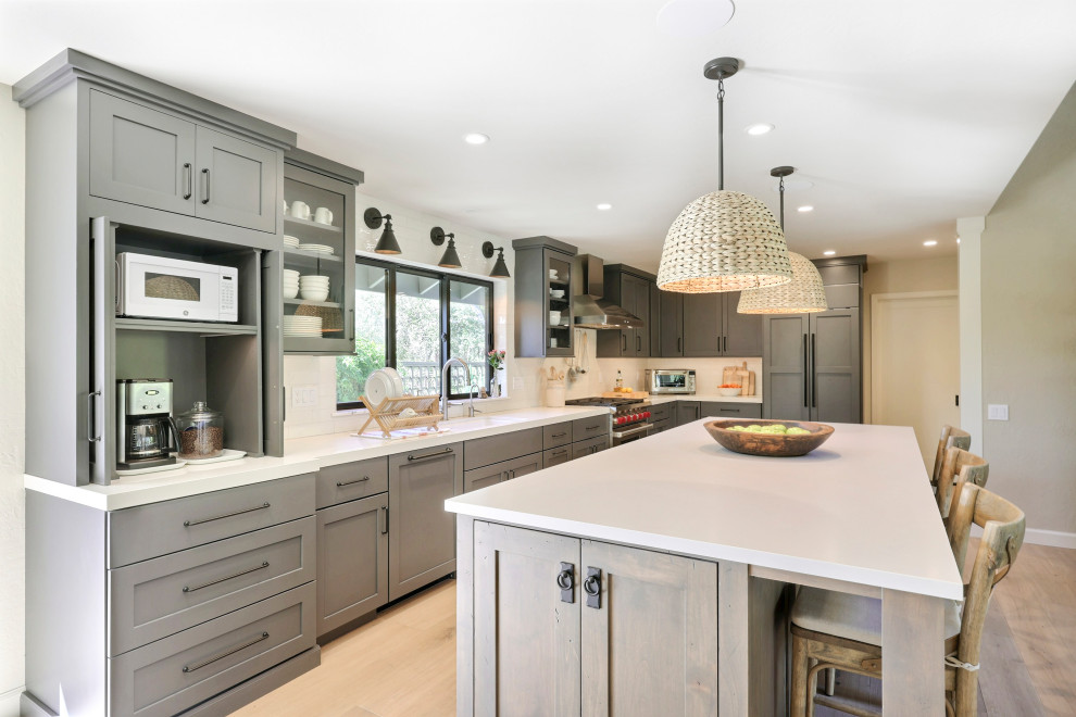 Mid-sized transitional l-shaped laminate floor open concept kitchen photo with a double-bowl sink, flat-panel cabinets, gray cabinets, quartz countertops, white backsplash, ceramic backsplash, stainless steel appliances, an island and white countertops