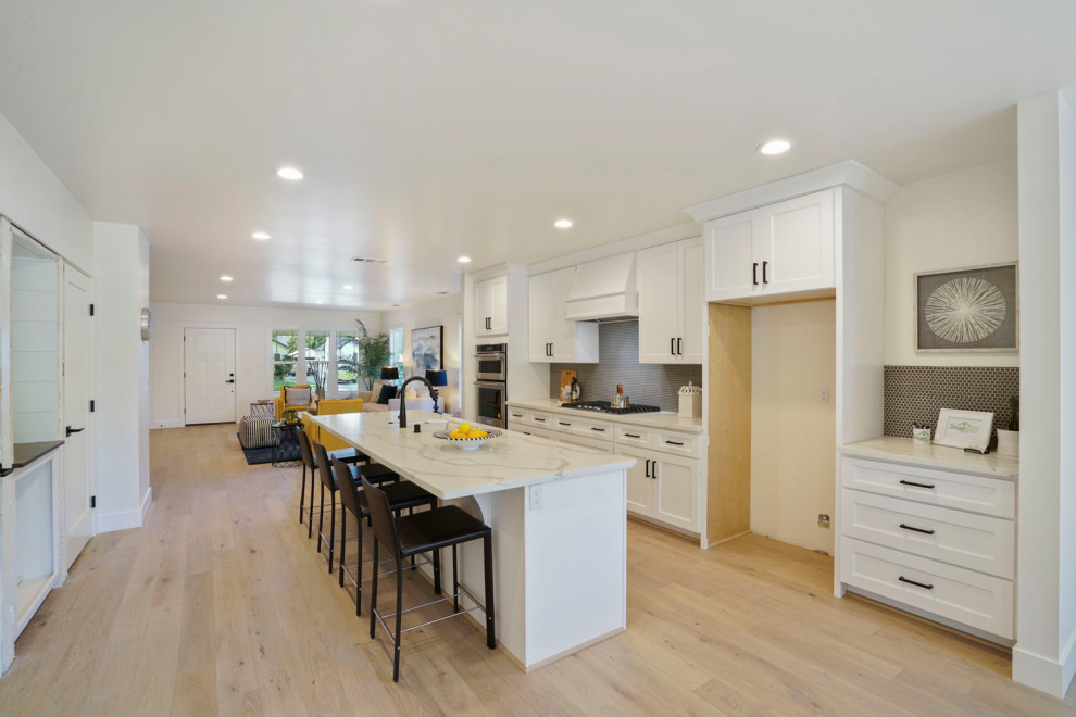 This is an example of a mid-sized country kitchen in Sacramento with an undermount sink, shaker cabinets, white cabinets, quartz benchtops, grey splashback, ceramic splashback, stainless steel appliances, light hardwood floors, with island and white benchtop.