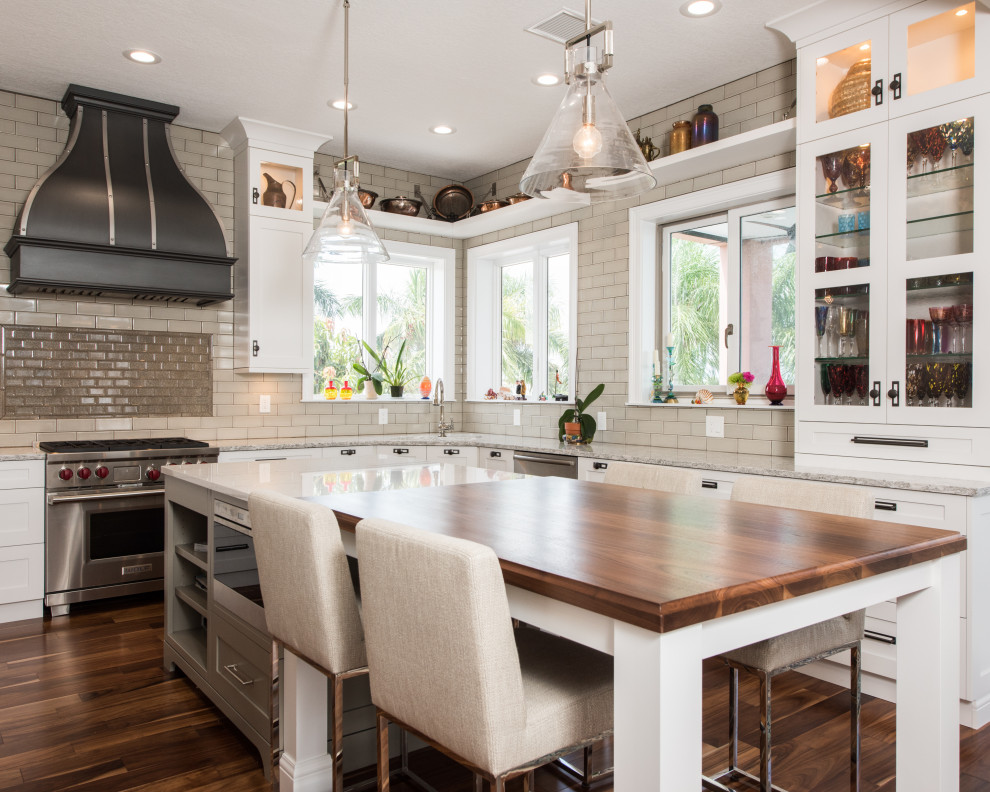 This is an example of a transitional l-shaped kitchen in Tampa with white cabinets, beige splashback, subway tile splashback, stainless steel appliances, dark hardwood floors, with island, brown floor, grey benchtop and shaker cabinets.