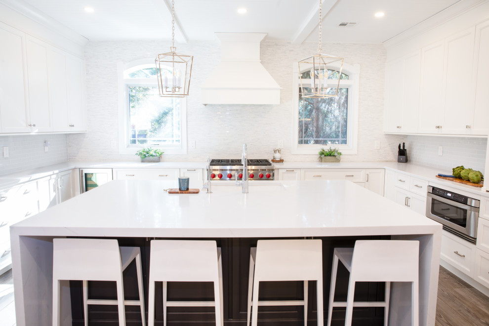 This is an example of a large transitional u-shaped eat-in kitchen in New York with an undermount sink, shaker cabinets, white cabinets, quartz benchtops, multi-coloured splashback, marble splashback, stainless steel appliances, with island, brown floor, white benchtop and timber.