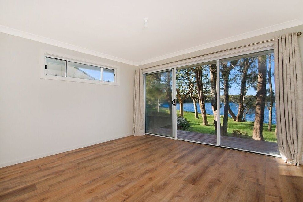 This is an example of a mid-sized beach style master bedroom in Sydney with beige walls and medium hardwood floors.