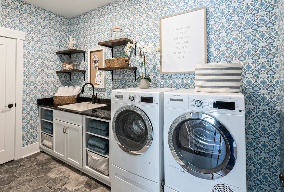 Inspiration for a transitional single-wall dedicated laundry room in Other with a drop-in sink, recessed-panel cabinets, white cabinets, blue walls, a side-by-side washer and dryer, grey floor and black benchtop.