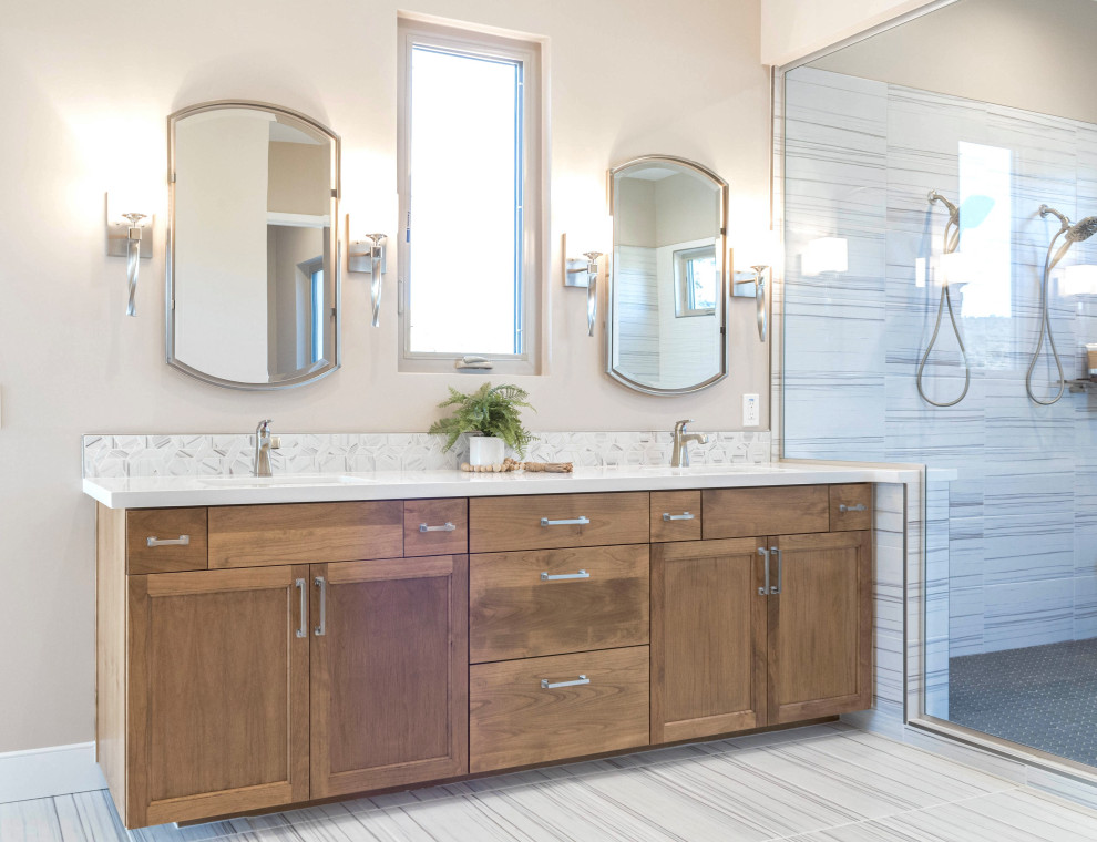 Пример оригинального дизайна: большая главная ванная комната в стиле неоклассика (современная классика) с фасадами в стиле шейкер, светлыми деревянными фасадами, отдельно стоящей ванной, душевой комнатой, унитазом-моноблоком, разноцветной плиткой, керамической плиткой, бежевыми стенами, полом из керамической плитки, врезной раковиной, столешницей из искусственного кварца, разноцветным полом, душем с распашными дверями, белой столешницей, сиденьем для душа, тумбой под две раковины и встроенной тумбой