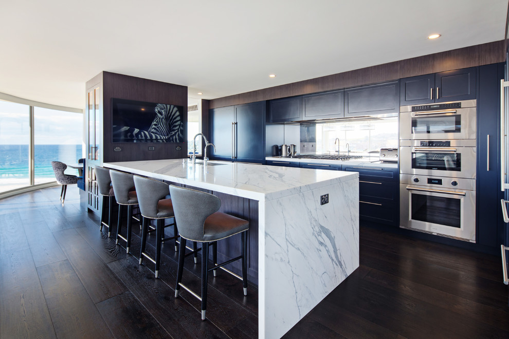 Design ideas for a large contemporary galley open plan kitchen in Sydney with an undermount sink, shaker cabinets, blue cabinets, marble benchtops, mirror splashback, stainless steel appliances, dark hardwood floors, with island and black floor.