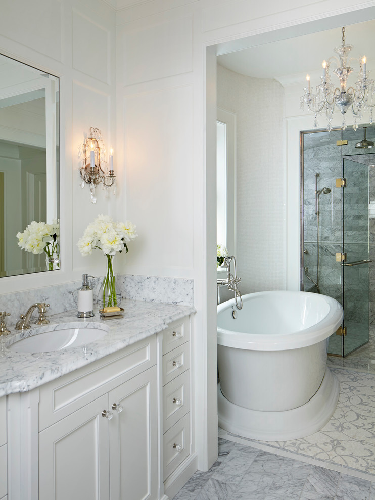 Expansive traditional master bathroom in Chicago with an undermount sink, recessed-panel cabinets, white cabinets, marble benchtops, a freestanding tub, a curbless shower, gray tile, stone tile, white walls and marble floors.