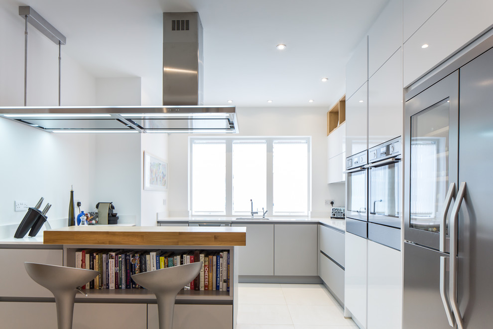 This is an example of a contemporary eat-in kitchen in Hertfordshire with flat-panel cabinets, quartzite benchtops and stainless steel appliances.