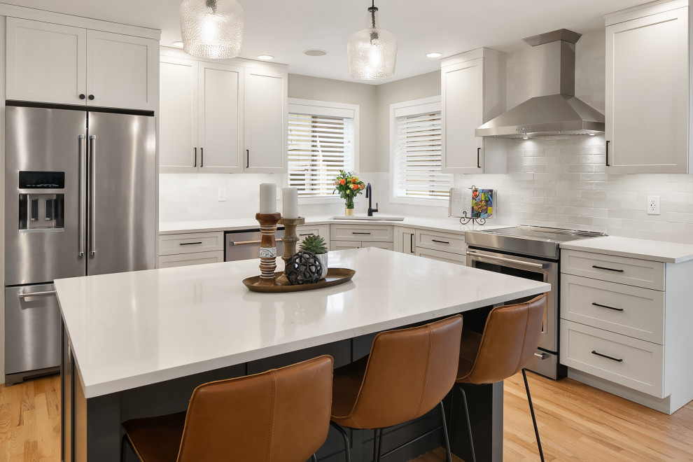 Small transitional l-shaped medium tone wood floor kitchen photo in Seattle with a single-bowl sink, shaker cabinets, white cabinets, quartz countertops, white backsplash, subway tile backsplash, stainless steel appliances, an island and white countertops