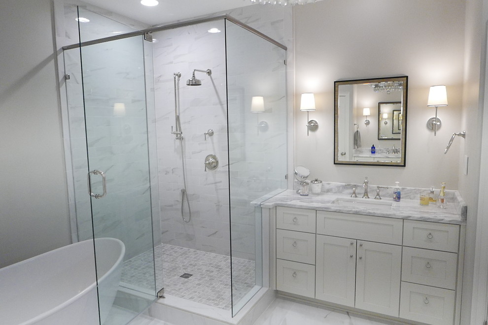 Large transitional master white tile and porcelain tile porcelain tile and white floor freestanding bathtub photo with shaker cabinets, white cabinets, a two-piece toilet, beige walls, an undermount sink, marble countertops, a hinged shower door and white countertops