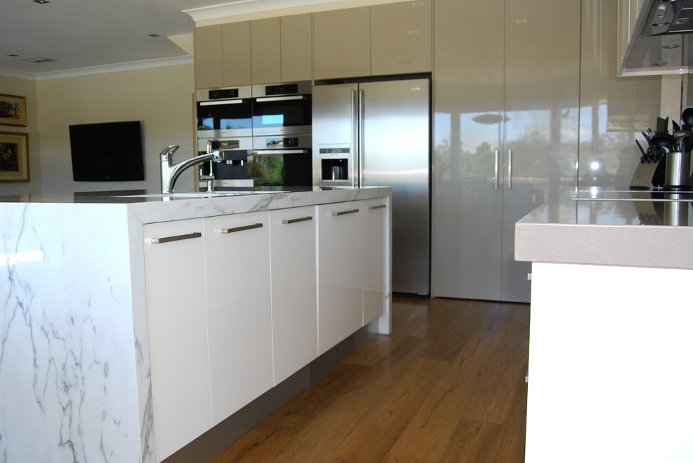 Photo of a large contemporary l-shaped kitchen pantry in Sydney with an undermount sink, flat-panel cabinets, white cabinets, marble benchtops, green splashback, glass sheet splashback, stainless steel appliances, medium hardwood floors and with island.