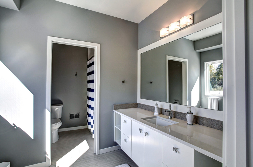 Inspiration for a large contemporary 3/4 bathroom in Grand Rapids with an undermount sink, white cabinets, engineered quartz benchtops, flat-panel cabinets, an alcove shower, a one-piece toilet, grey walls and porcelain floors.