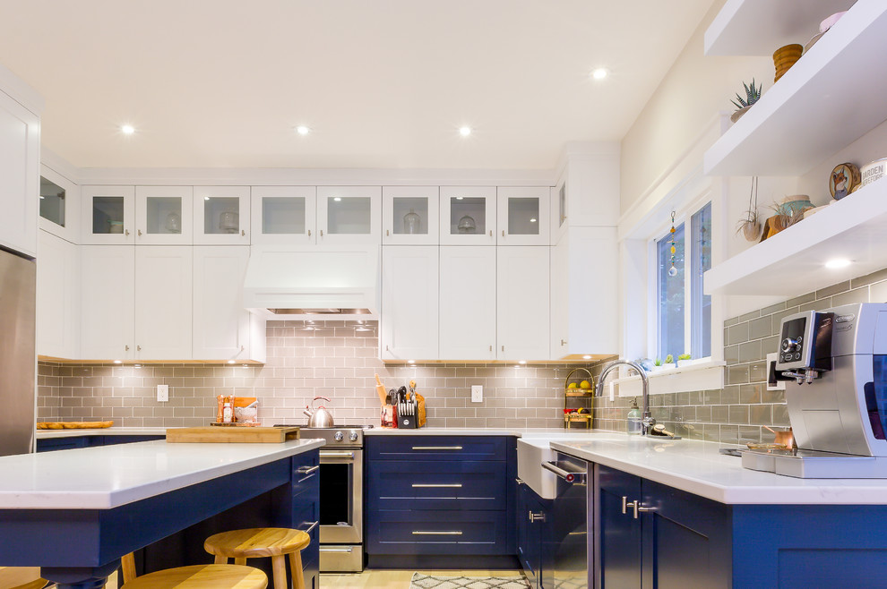 Example of a large transitional u-shaped light wood floor open concept kitchen design with a farmhouse sink, shaker cabinets, blue cabinets, quartz countertops, gray backsplash, glass tile backsplash, stainless steel appliances, an island and white countertops
