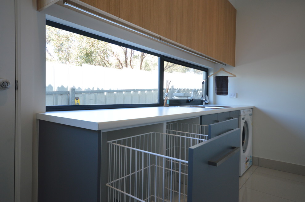 Mid-sized modern l-shaped dedicated laundry room in Adelaide with a single-bowl sink, light wood cabinets, laminate benchtops, white walls and porcelain floors.