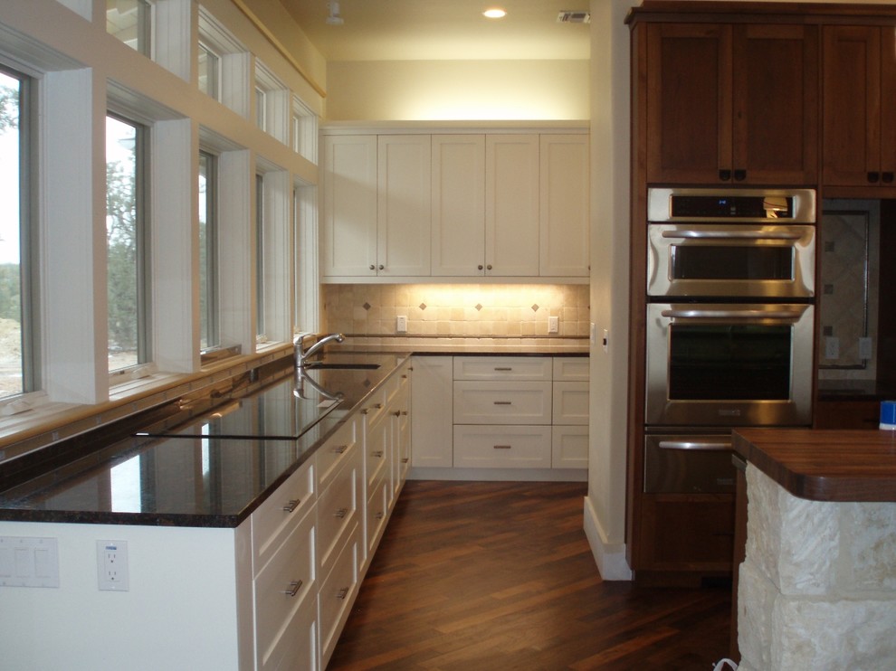 Photo of a large transitional l-shaped eat-in kitchen in Austin with an undermount sink, shaker cabinets, white cabinets, granite benchtops, beige splashback, cement tile splashback, stainless steel appliances, dark hardwood floors and with island.