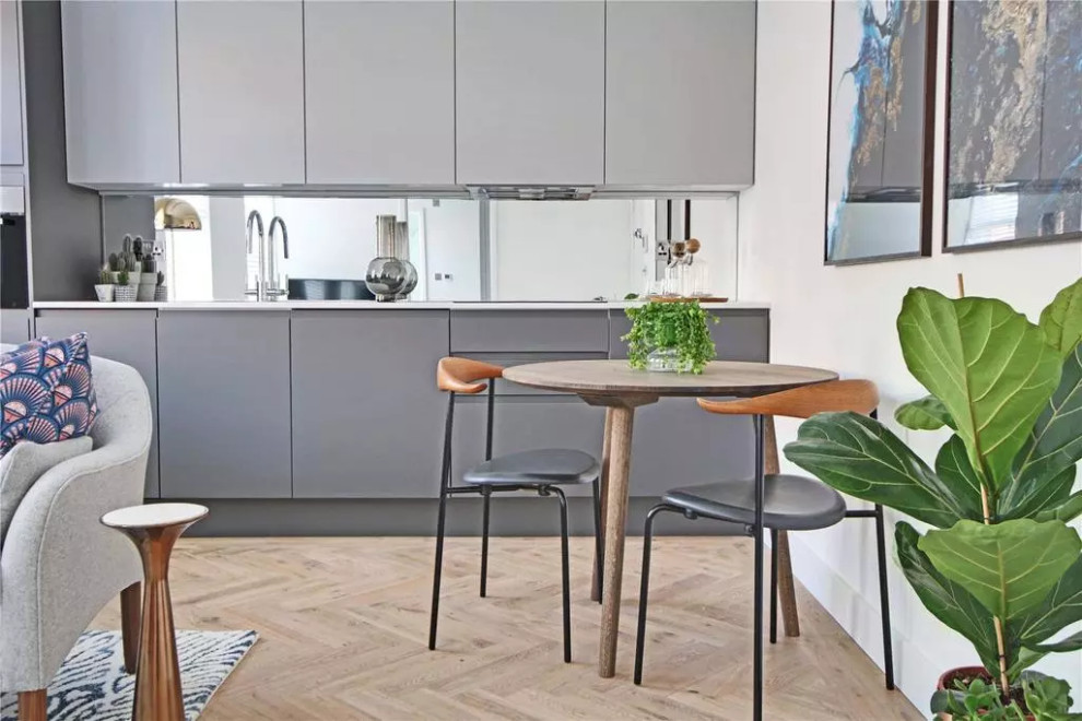 This is an example of a small contemporary single-wall open plan kitchen in London with an integrated sink, flat-panel cabinets, grey cabinets, quartzite benchtops, grey splashback, glass sheet splashback, panelled appliances, light hardwood floors, no island, brown floor, white benchtop and coffered.