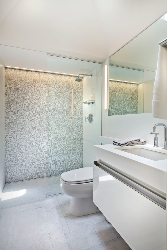 This is an example of a small contemporary 3/4 bathroom in Minneapolis with an undermount sink, white cabinets, an alcove shower, white tile, solid surface benchtops, a one-piece toilet, porcelain floors and flat-panel cabinets.
