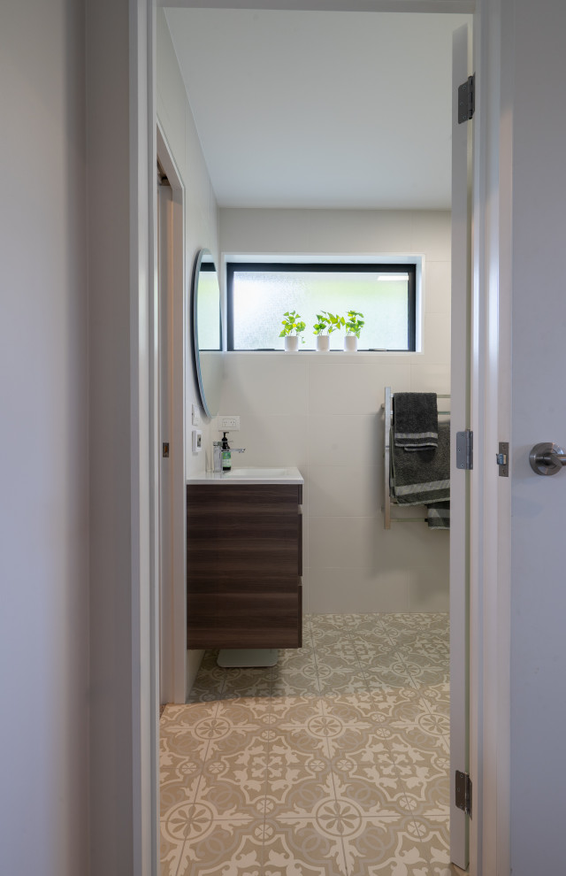 Inspiration for a mid-sized contemporary master bathroom in Auckland with recessed-panel cabinets, brown cabinets, a corner shower, a one-piece toilet, white tile, ceramic tile, white walls, ceramic floors, an integrated sink, engineered quartz benchtops, beige floor, a sliding shower screen, a single vanity and a floating vanity.