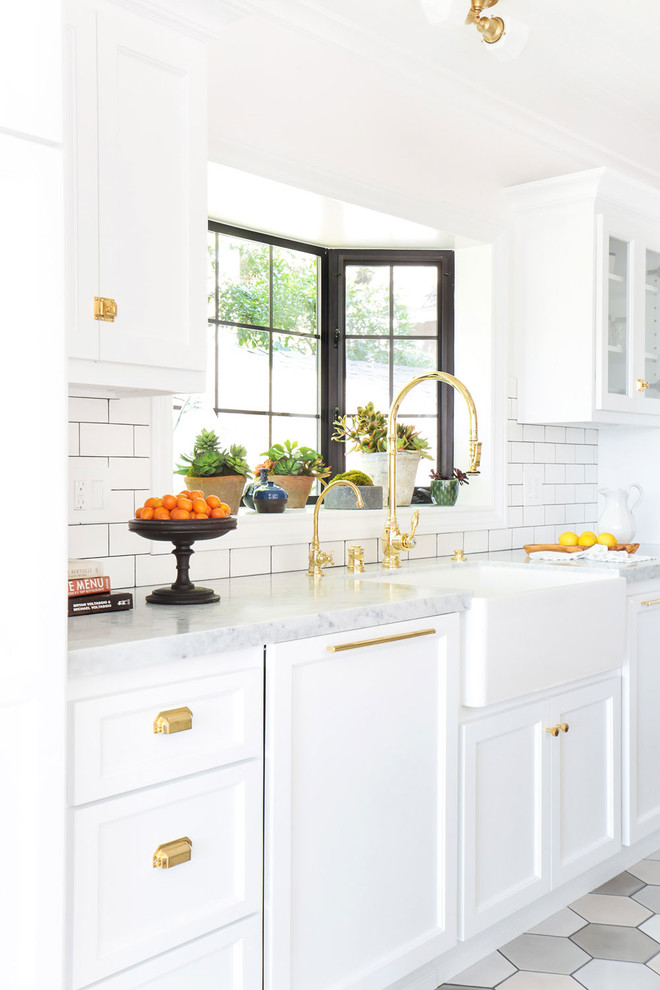 This is an example of a large country u-shaped open plan kitchen in Los Angeles with a farmhouse sink, recessed-panel cabinets, white cabinets, marble benchtops, white splashback, subway tile splashback, white appliances, ceramic floors and a peninsula.
