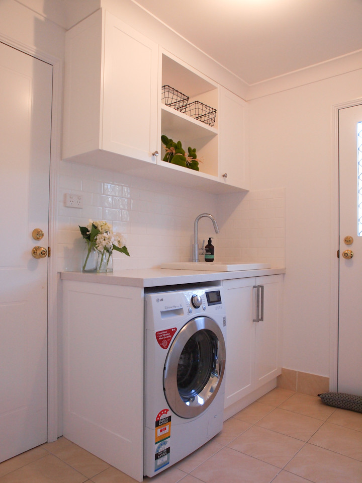 Small traditional single-wall dedicated laundry room in Wollongong with a drop-in sink, white cabinets, granite benchtops, white walls, porcelain floors and recessed-panel cabinets.