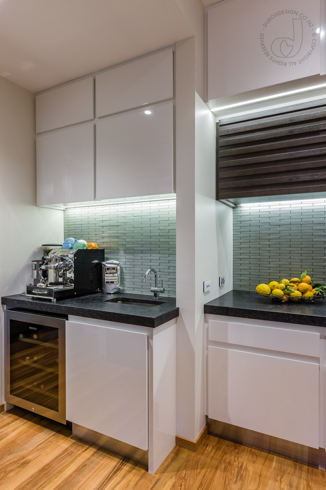 Photo of a mid-sized contemporary galley eat-in kitchen in Auckland with a double-bowl sink, louvered cabinets, dark wood cabinets, quartzite benchtops, green splashback, glass tile splashback, stainless steel appliances, light hardwood floors and with island.