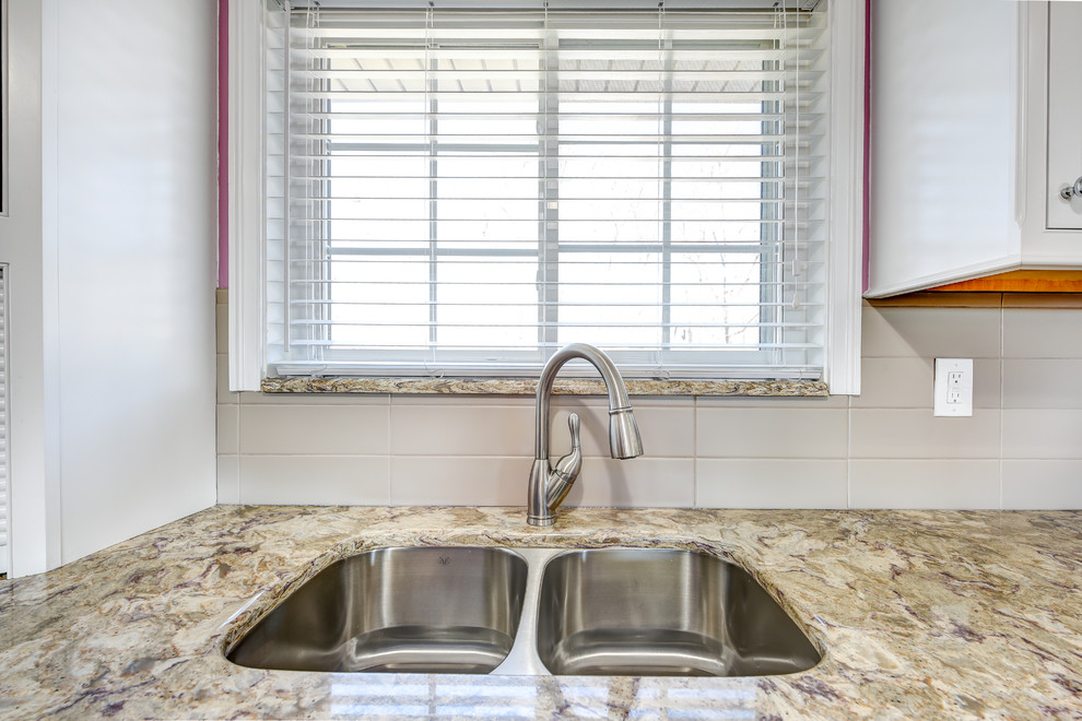Example of a mid-sized classic u-shaped ceramic tile eat-in kitchen design with an undermount sink, recessed-panel cabinets, white cabinets, granite countertops, beige backsplash, ceramic backsplash, stainless steel appliances and no island