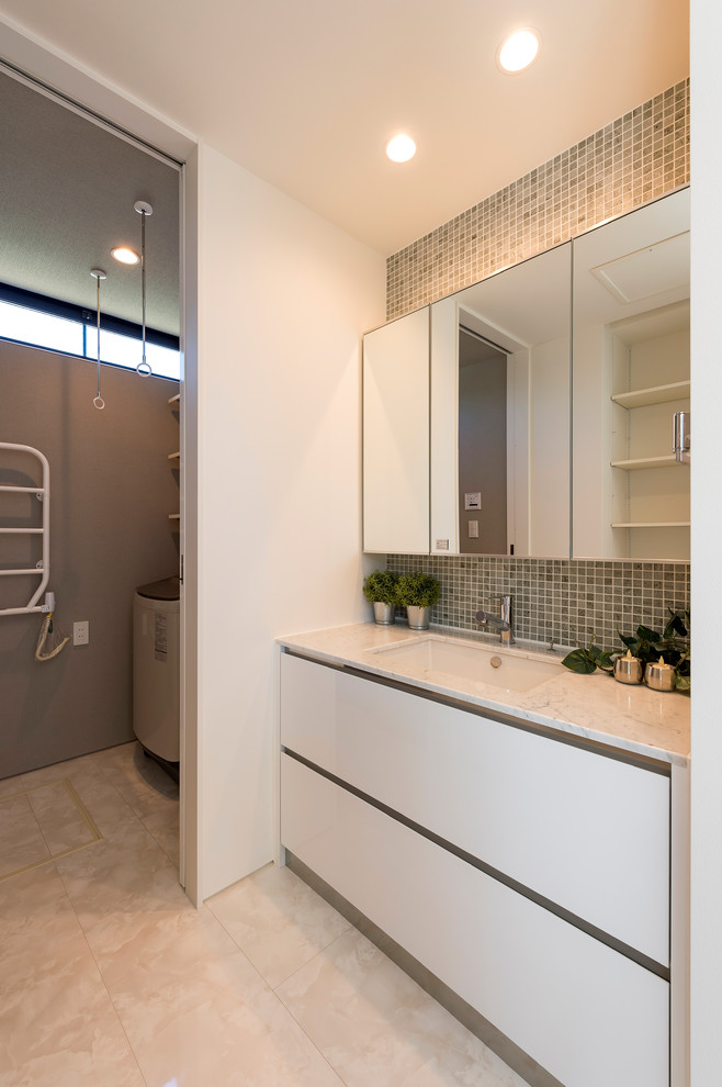 This is an example of a modern powder room in Other with flat-panel cabinets, white cabinets, gray tile, white walls, an integrated sink and beige floor.