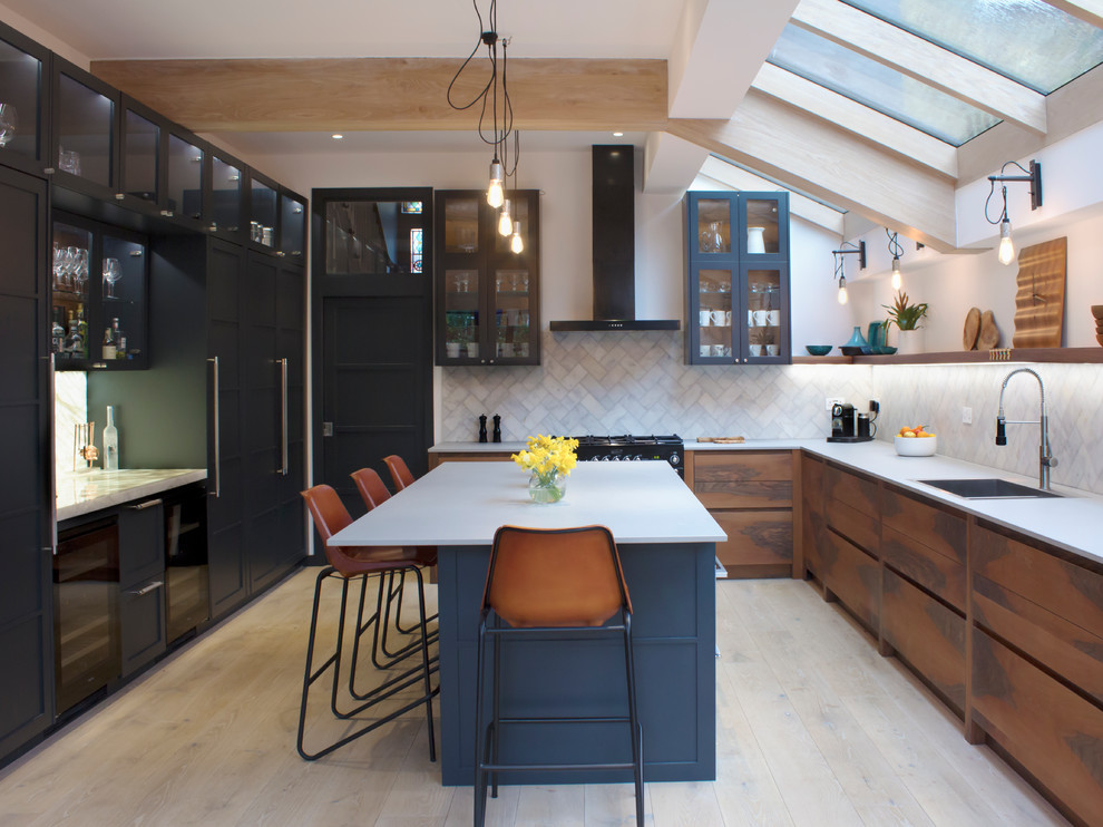 Inspiration for a mid-sized transitional l-shaped separate kitchen in London with flat-panel cabinets, medium wood cabinets, light hardwood floors, with island, white splashback, black appliances and beige floor.