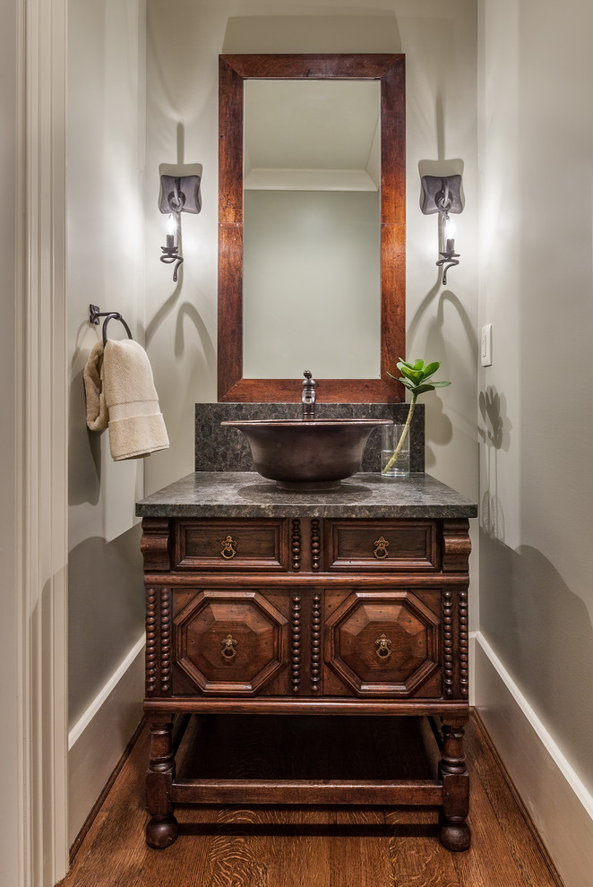Design ideas for a mid-sized mediterranean powder room in Other with furniture-like cabinets, beige walls, medium hardwood floors, a vessel sink, dark wood cabinets, a one-piece toilet, granite benchtops, brown floor and gray tile.