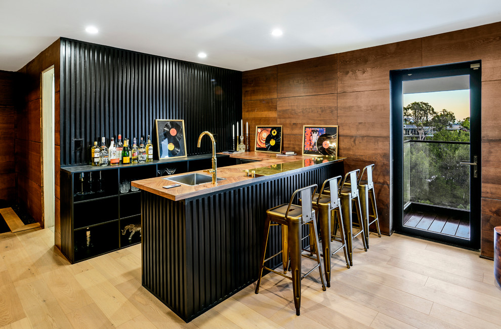 Mid-sized contemporary u-shaped wet bar in Los Angeles with black cabinets, black splashback, timber splashback, light hardwood floors and brown benchtop.