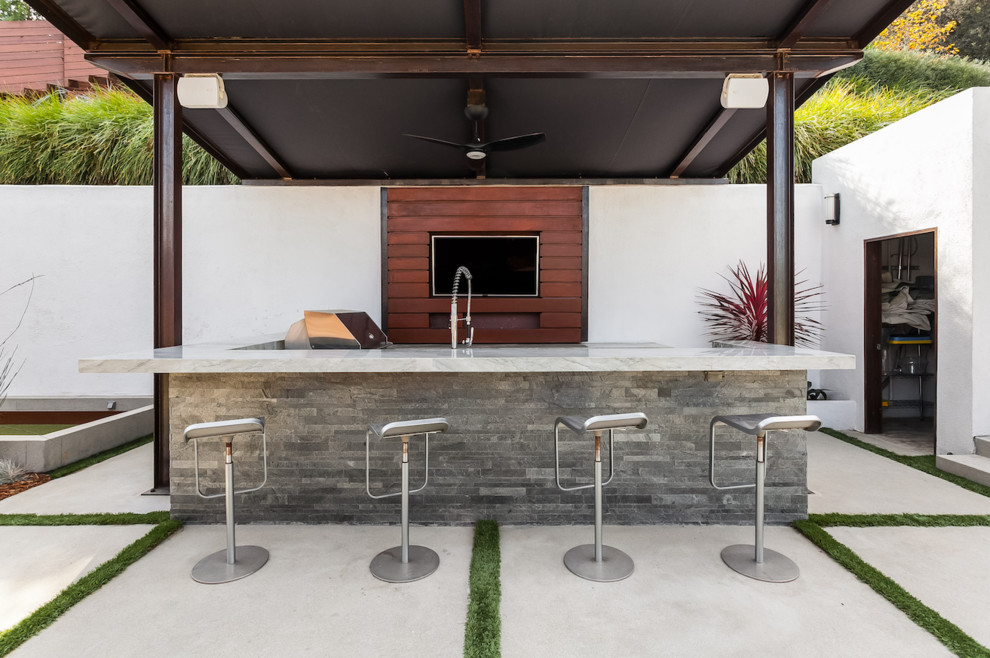 This is an example of a large modern backyard patio in Los Angeles with an outdoor kitchen, an awning and concrete pavers.