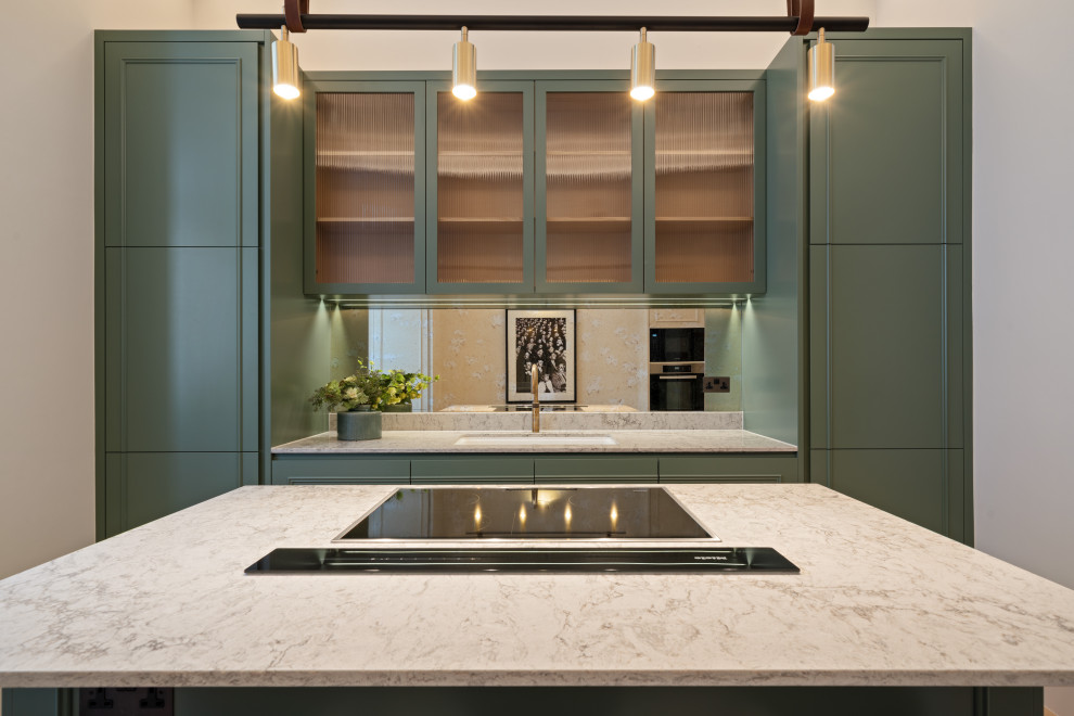 This is an example of a mid-sized transitional kitchen in London with an undermount sink, glass-front cabinets, green cabinets, quartz benchtops, mirror splashback, panelled appliances, with island and beige benchtop.