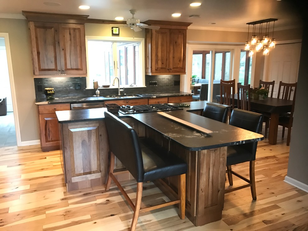 Photo of a large country l-shaped eat-in kitchen in Other with an undermount sink, raised-panel cabinets, medium wood cabinets, granite benchtops, grey splashback, ceramic splashback, stainless steel appliances, light hardwood floors, with island and beige floor.
