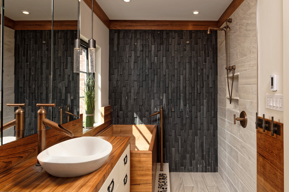 Inspiration for a mid-sized asian master bathroom in DC Metro with white cabinets, a japanese tub, a one-piece toilet, porcelain floors, a vessel sink, wood benchtops, flat-panel cabinets, an open shower, black tile, stone tile, beige walls and brown benchtops.