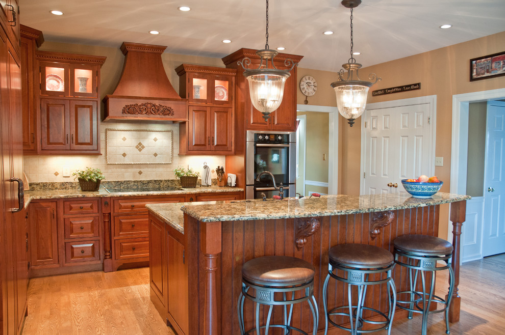 Traditional l-shaped eat-in kitchen in Philadelphia with raised-panel cabinets, medium wood cabinets, beige splashback, stainless steel appliances, light hardwood floors, with island and a double-bowl sink.