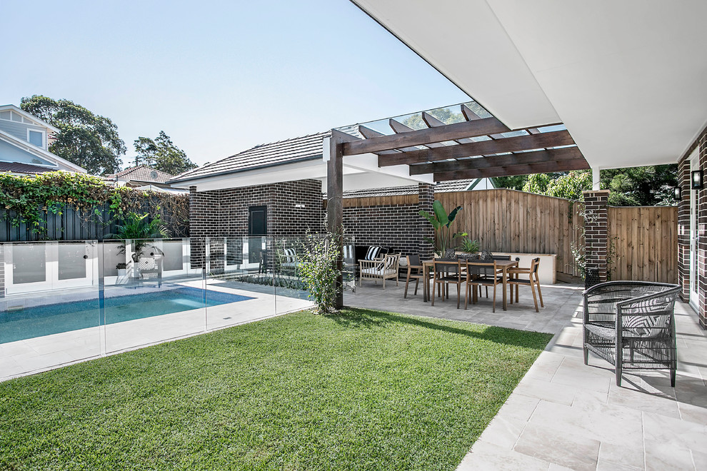 This is an example of a mid-sized transitional backyard rectangular lap pool in Sydney with a pool house and natural stone pavers.