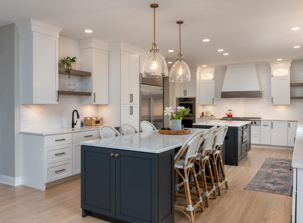 Eat-in kitchen - huge transitional galley light wood floor and gray floor eat-in kitchen idea with a farmhouse sink, recessed-panel cabinets, white cabinets, quartz countertops, white backsplash, subway tile backsplash, stainless steel appliances, two islands and white countertops
