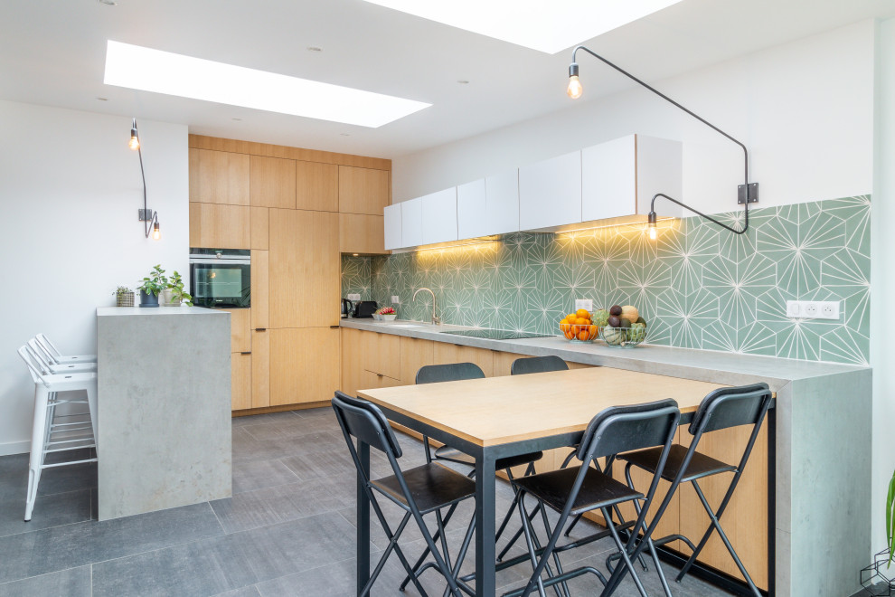 Photo of a mid-sized contemporary u-shaped open plan kitchen in Lille with an undermount sink, light wood cabinets, green splashback, grey floor, grey benchtop, beaded inset cabinets, tile benchtops, cement tile splashback, black appliances, ceramic floors and with island.