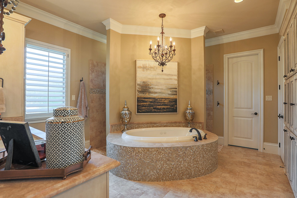 This is an example of a large mediterranean master bathroom in Dallas with raised-panel cabinets, beige cabinets, a drop-in tub, an open shower, a one-piece toilet, beige tile, ceramic tile, beige walls, ceramic floors, an undermount sink, marble benchtops, beige floor, an open shower and beige benchtops.