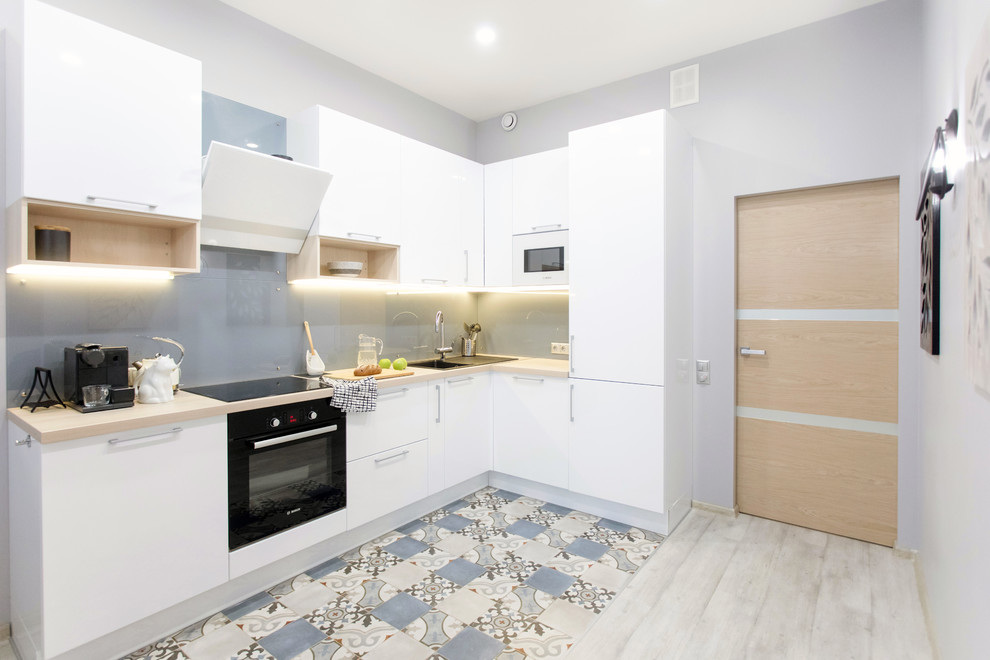 Photo of a mid-sized scandinavian l-shaped eat-in kitchen in Saint Petersburg with a single-bowl sink, flat-panel cabinets, white cabinets, blue splashback, glass sheet splashback, black appliances, porcelain floors, no island, multi-coloured floor and beige benchtop.