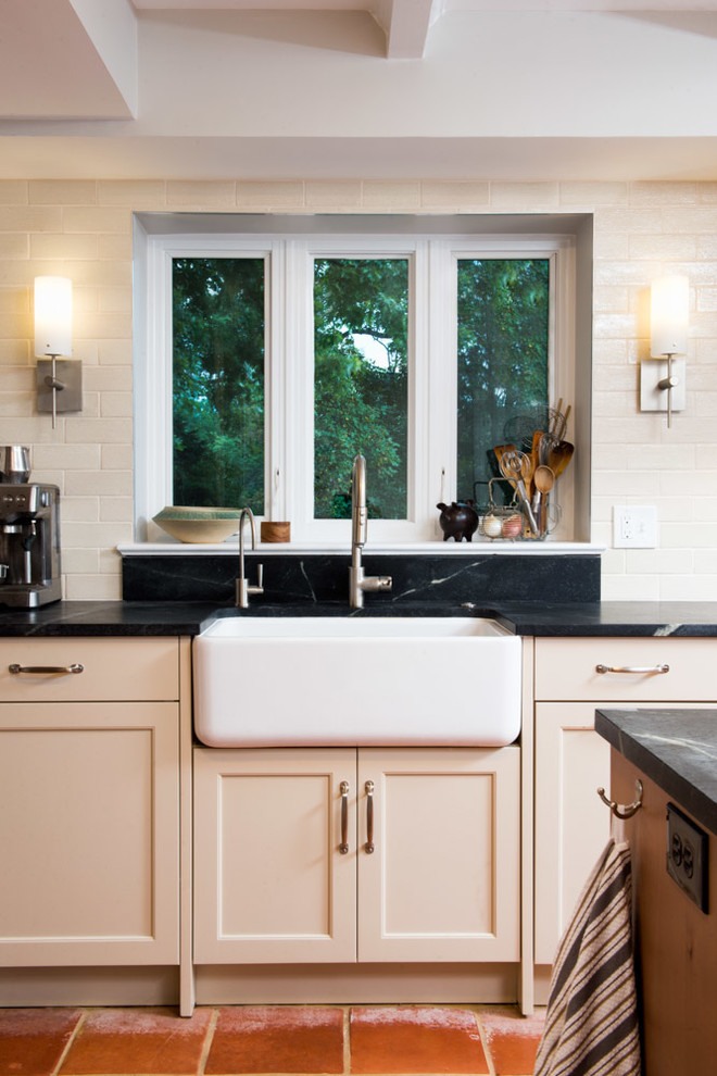 Transitional l-shaped eat-in kitchen photo in DC Metro with a farmhouse sink, shaker cabinets, beige cabinets, soapstone countertops, black backsplash, ceramic backsplash and stainless steel appliances