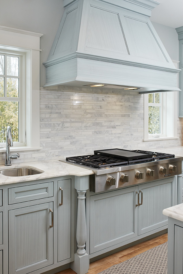 Inspiration for a large beach style u-shaped open plan kitchen in Grand Rapids with a triple-bowl sink, beaded inset cabinets, blue cabinets, marble benchtops, white splashback, stone tile splashback, panelled appliances, medium hardwood floors and with island.