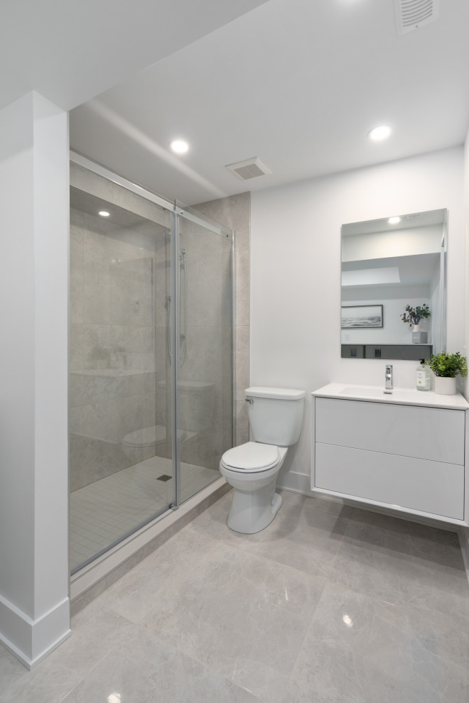 This is an example of a medium sized modern shower room bathroom in Montreal with flat-panel cabinets, white cabinets, an alcove shower, a one-piece toilet, grey tiles, ceramic tiles, white walls, ceramic flooring, a submerged sink, engineered stone worktops, grey floors, a sliding door, white worktops, a laundry area, a single sink and a floating vanity unit.