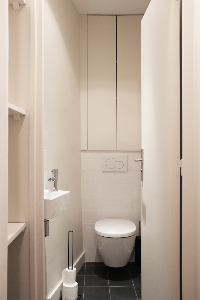 Exemple d'un petit WC suspendu éclectique avec un placard à porte affleurante, des portes de placard blanches, un carrelage blanc, des carreaux de céramique, meuble-lavabo encastré, un mur blanc, carreaux de ciment au sol, un lavabo suspendu et un sol gris.