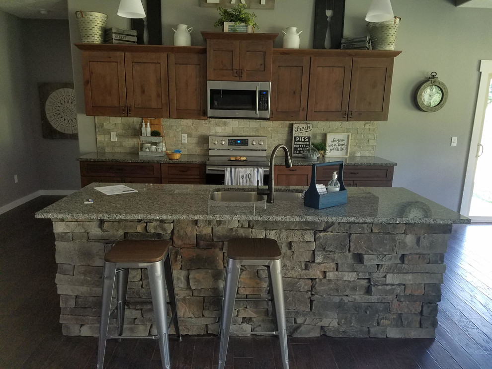 Mid-sized mountain style single-wall dark wood floor and brown floor open concept kitchen photo with an undermount sink, shaker cabinets, dark wood cabinets, granite countertops, beige backsplash, stone tile backsplash, stainless steel appliances and an island