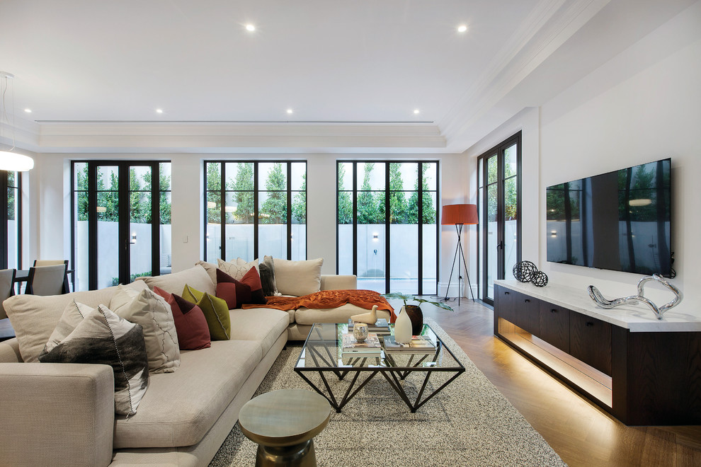 This is an example of a contemporary formal open concept living room in Melbourne with white walls, medium hardwood floors, a wall-mounted tv and beige floor.