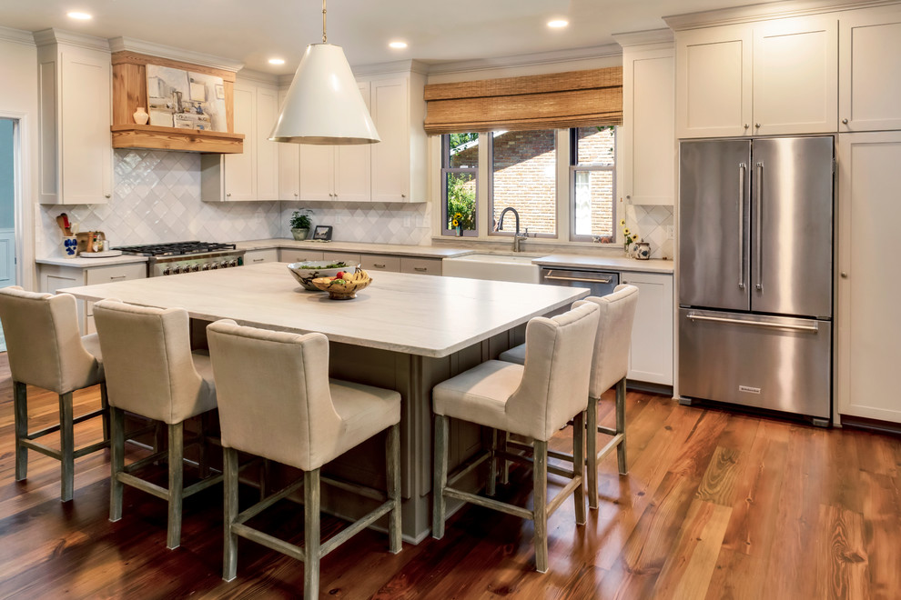Design ideas for a mid-sized transitional l-shaped eat-in kitchen in New Orleans with a farmhouse sink, recessed-panel cabinets, beige cabinets, grey splashback, stainless steel appliances, medium hardwood floors, with island, brown floor and grey benchtop.